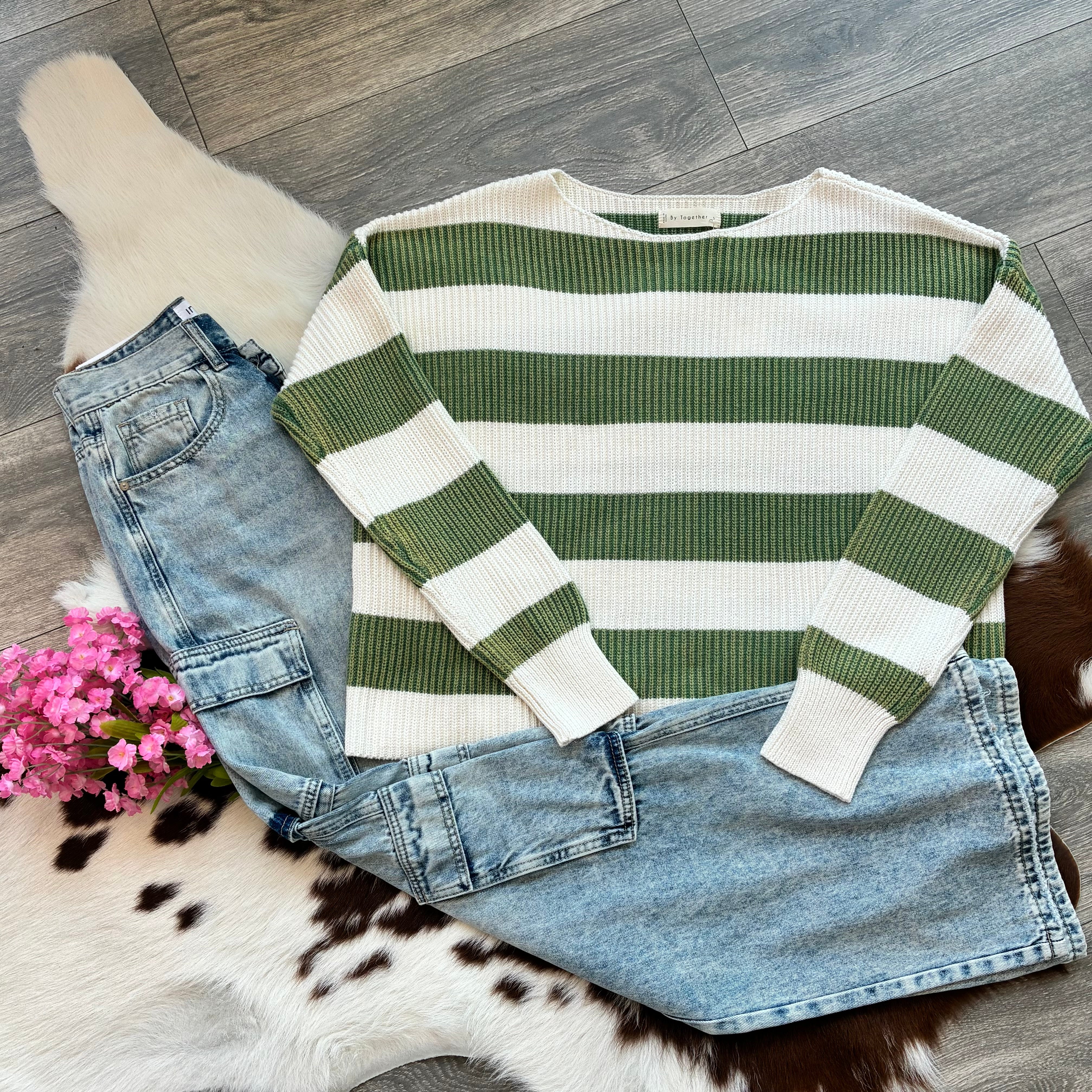 Green and white striped sweater with blue jeans on a wooden floor.