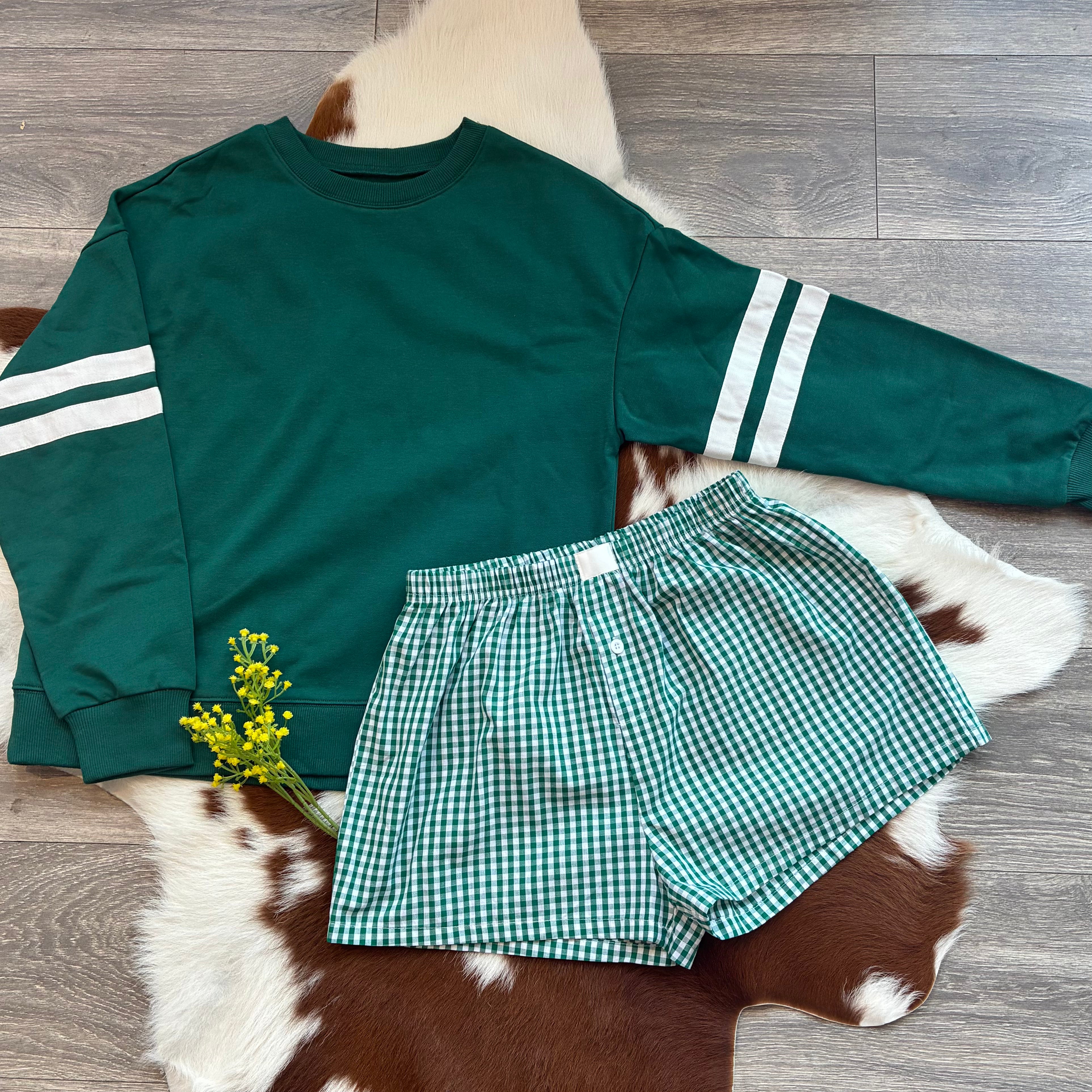 Green sweatshirt with white stripes and green checkered shorts on a cowhide rug.