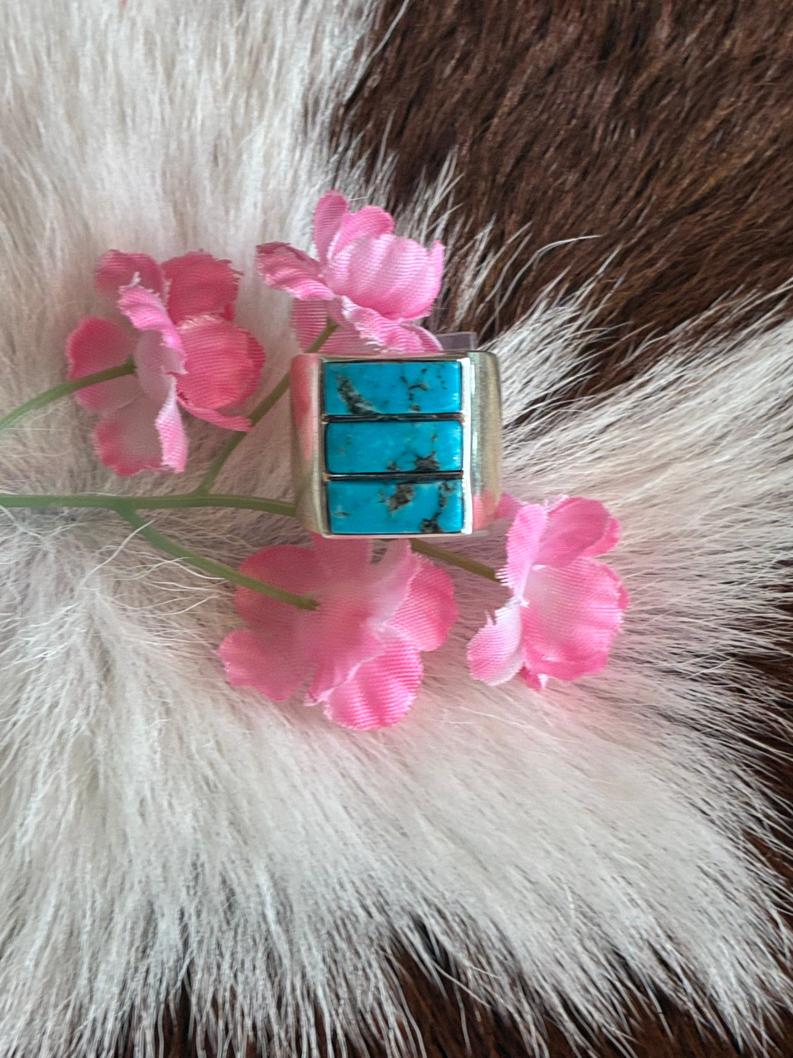 Cut turquoise statement ring featuring three vibrant turquoise stones on a silver band, surrounded by pink flowers on a soft fur background.