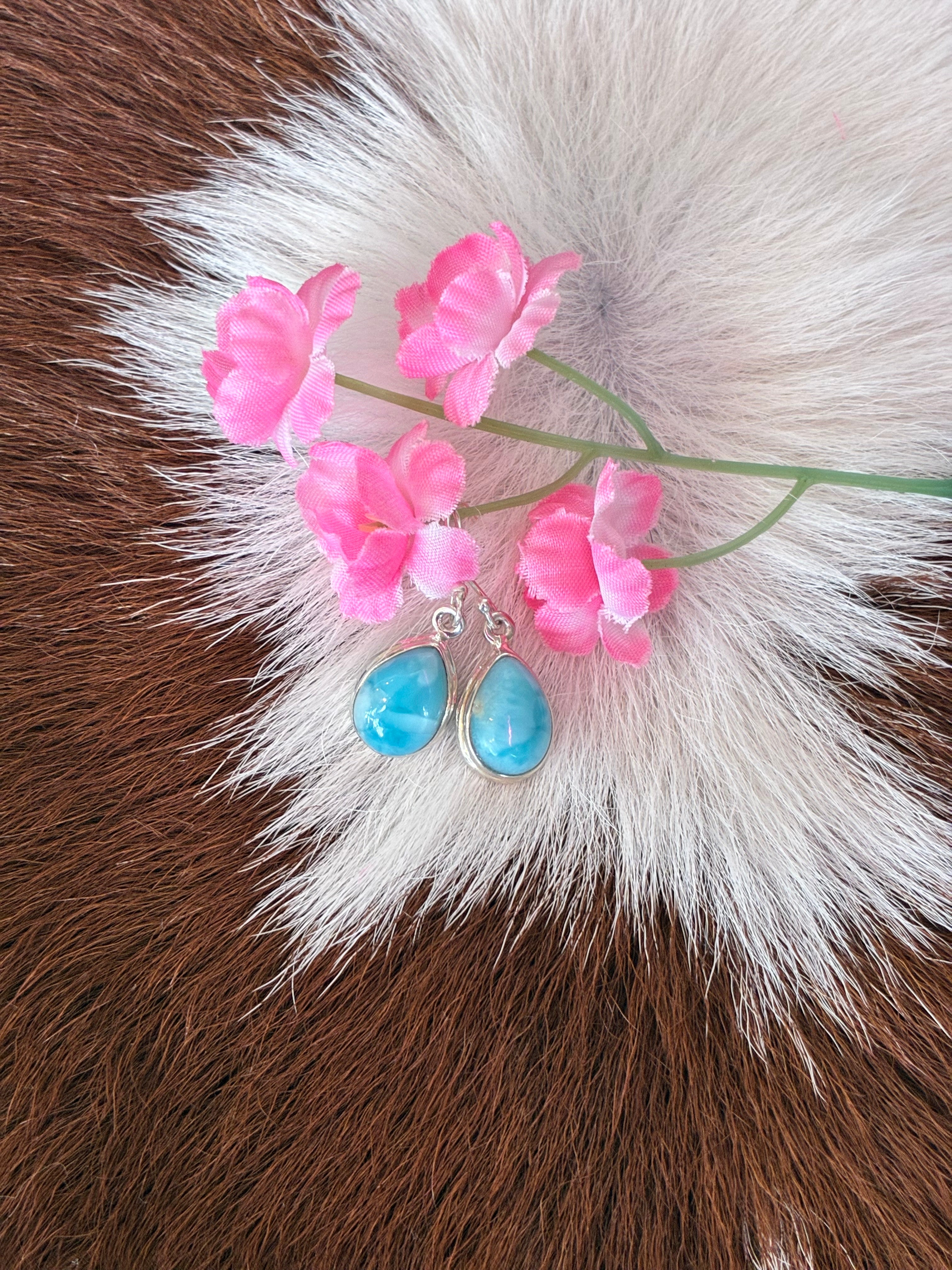 Teardrop Larimar earrings with vibrant blue hues set in silver, surrounded by pink flowers on a textured fur background.