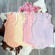 Flat lay of four adult-sized ribbed tank tops in pastel striped colors—orange, yellow, pink, and lavender—arranged side by side on a cowhide rug with pink faux flowers placed above, displayed on a wood floor background.