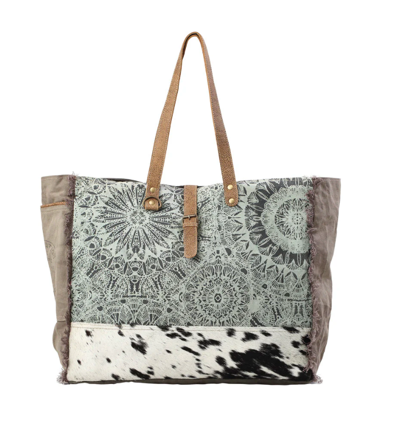 Green floral mandala print weekender tote with brown leather handles and a black-and-white cowhide panel on the bottom.