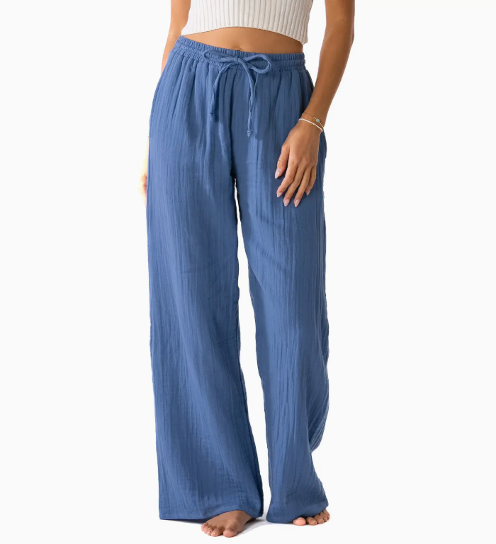 A woman wearing blue wide-leg pants with an adjustable drawstring waist, posing in a relaxed manner. She is paired with a fitted crop top, showcasing a casual and stylish look against a white background. The pants feature a flowy design, perfect for warm weather and comfortable outings.