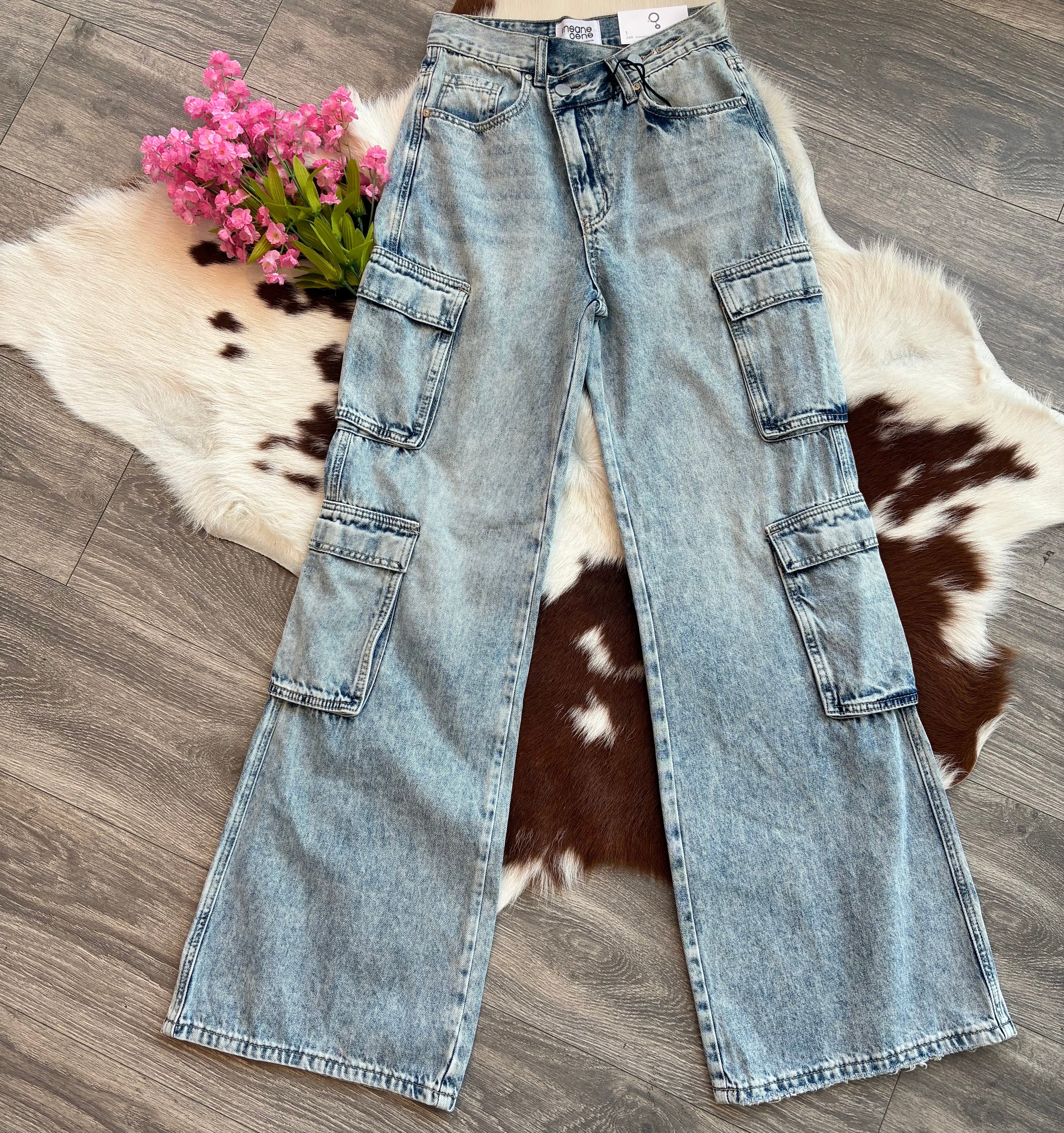 Light blue jeans on a wooden floor with a cowhide rug and pink flowers.