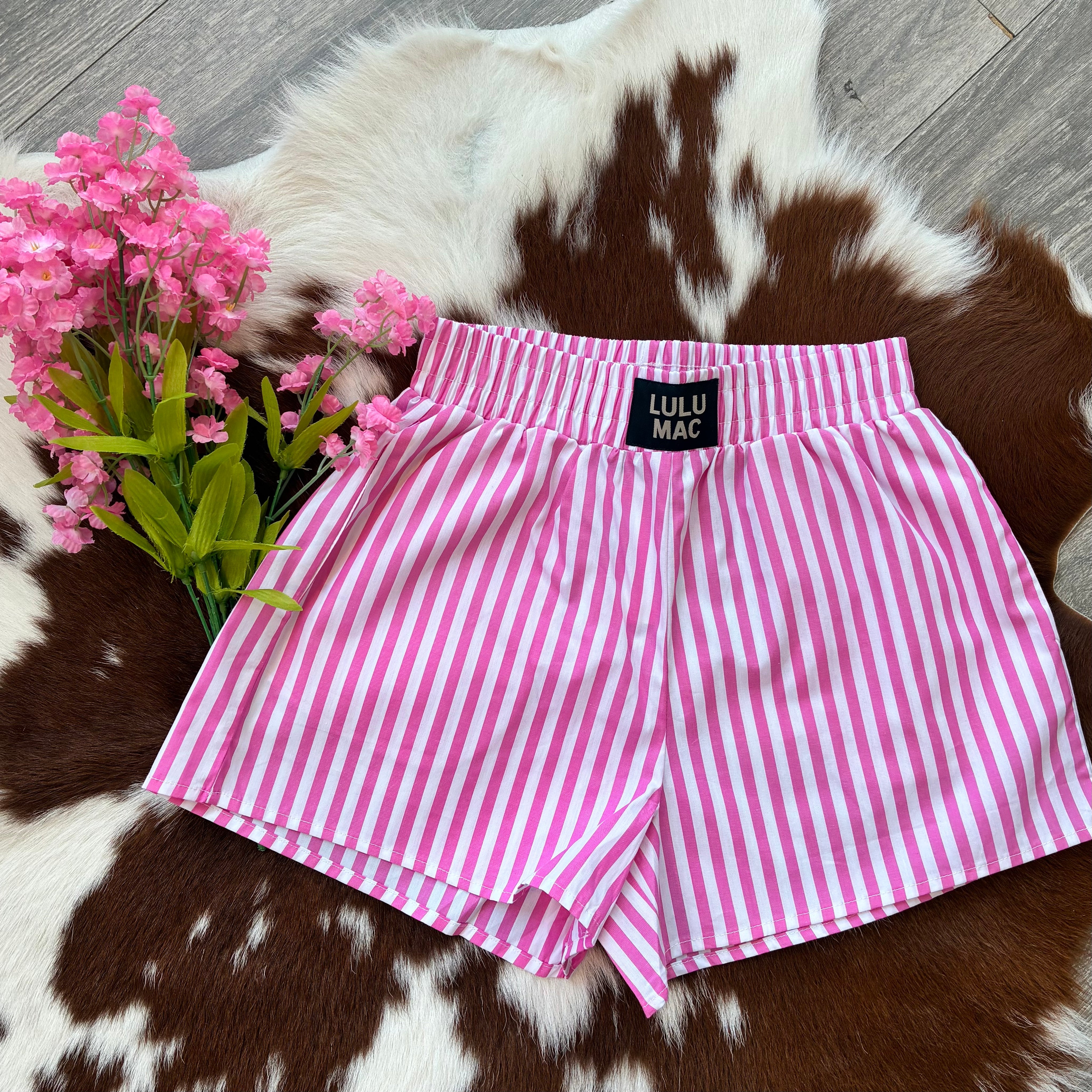Pink and white striped shorts with 'Lulu Mac' label on a cowhide rug with pink flowers.