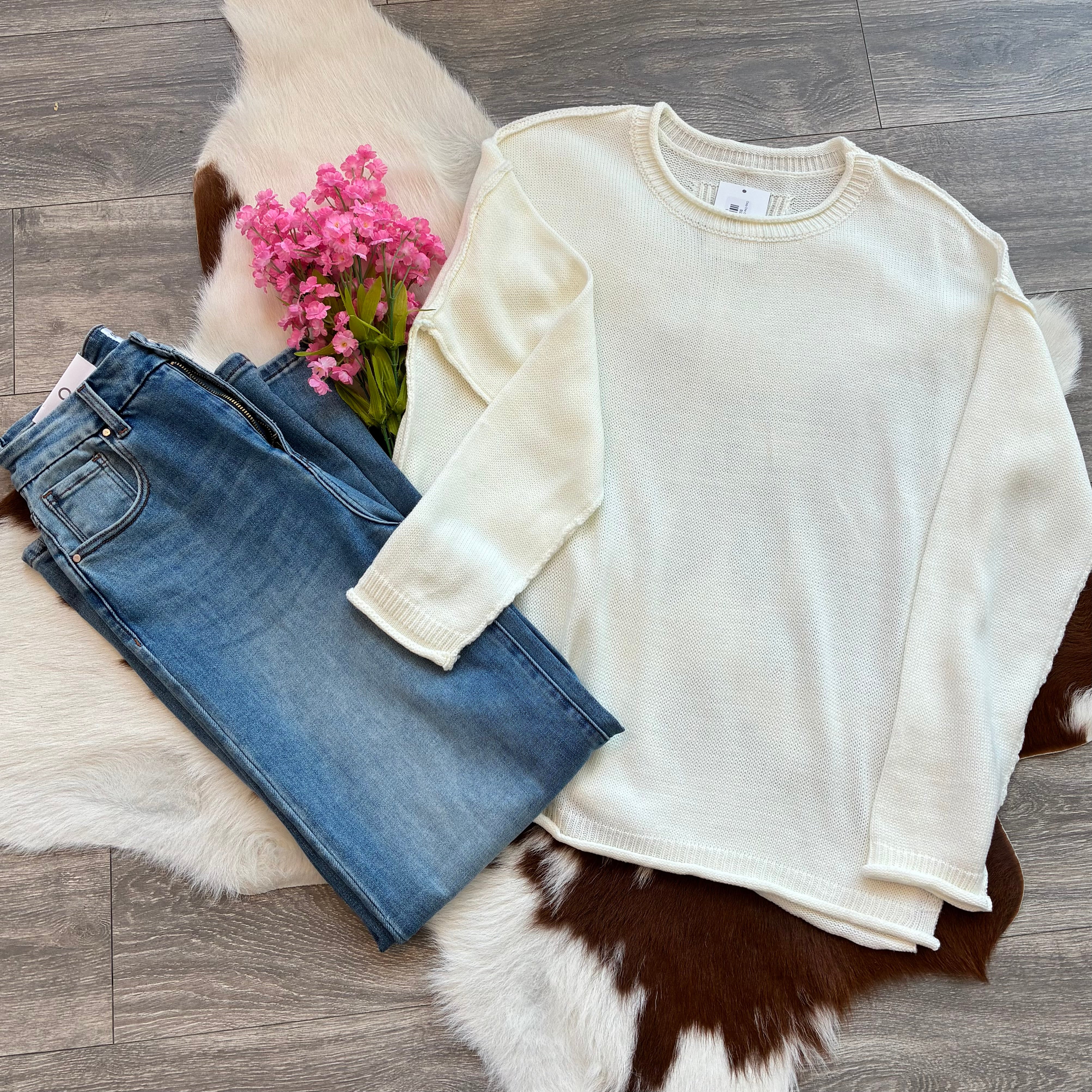 White sweater and blue jeans on a fur surface with pink flowers.