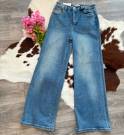 Blue jeans on a wooden floor with a cowhide rug and pink flowers.