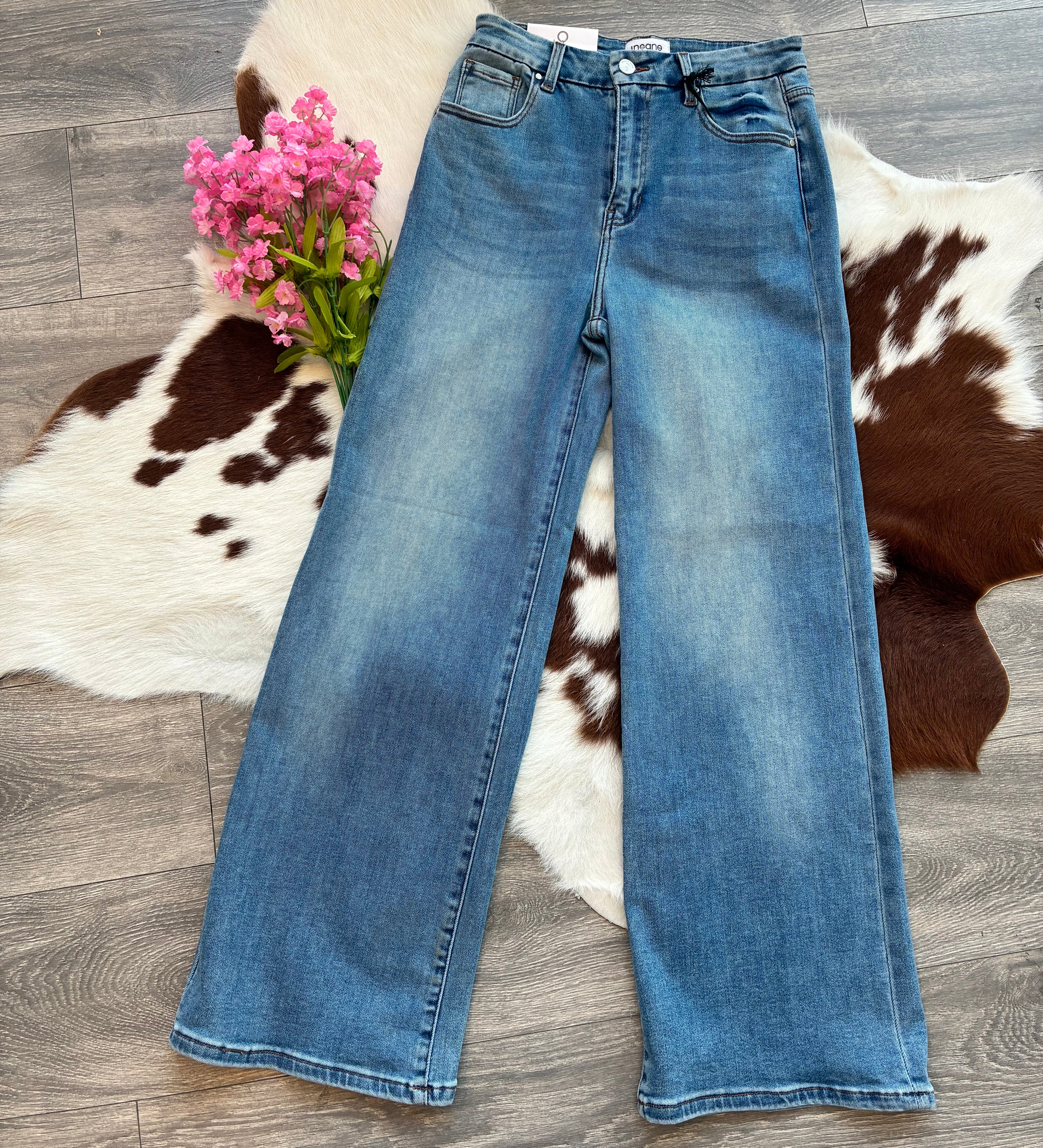 Blue jeans on a wooden floor with a cowhide rug and pink flowers.