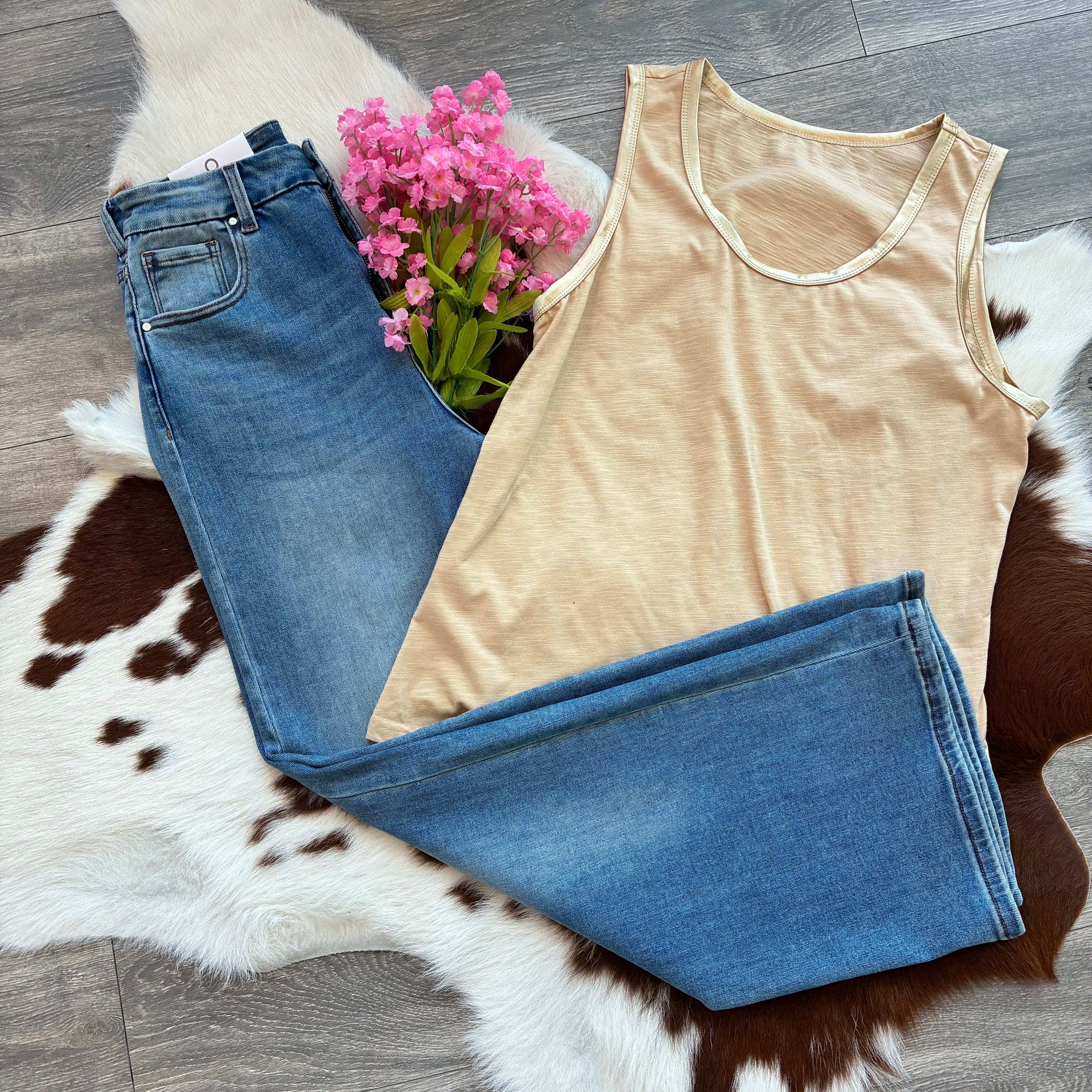 Beige tank top and blue jeans on a cowhide rug with pink flowers.