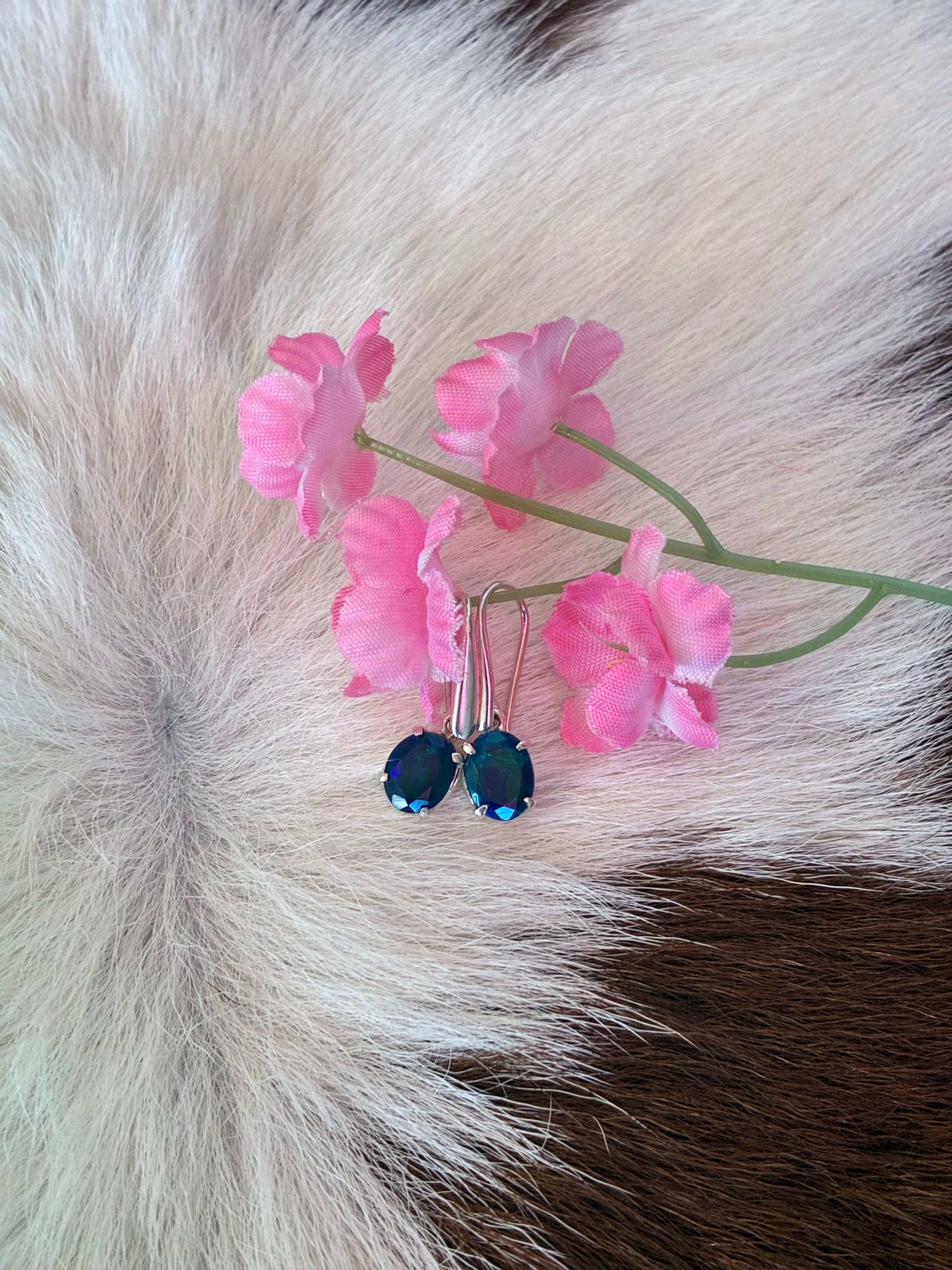Black Ethiopian opal earrings with vibrant green and blue hues set in silver, placed on a textured fur background with pink floral accents.