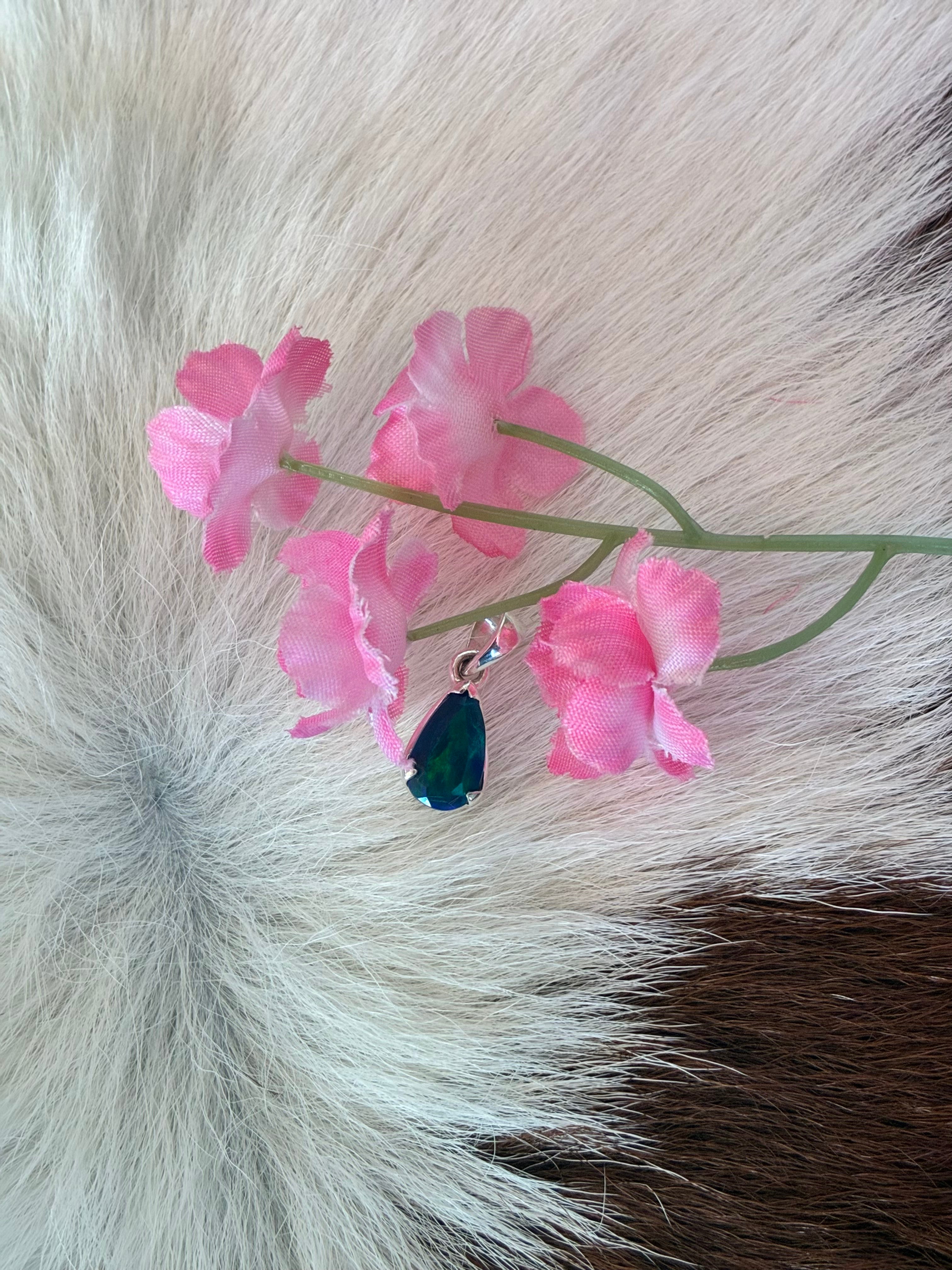 Black Ethiopian opal teardrop pendant in silver setting, displaying vibrant green and blue hues, surrounded by pink floral accents on a textured fur background.