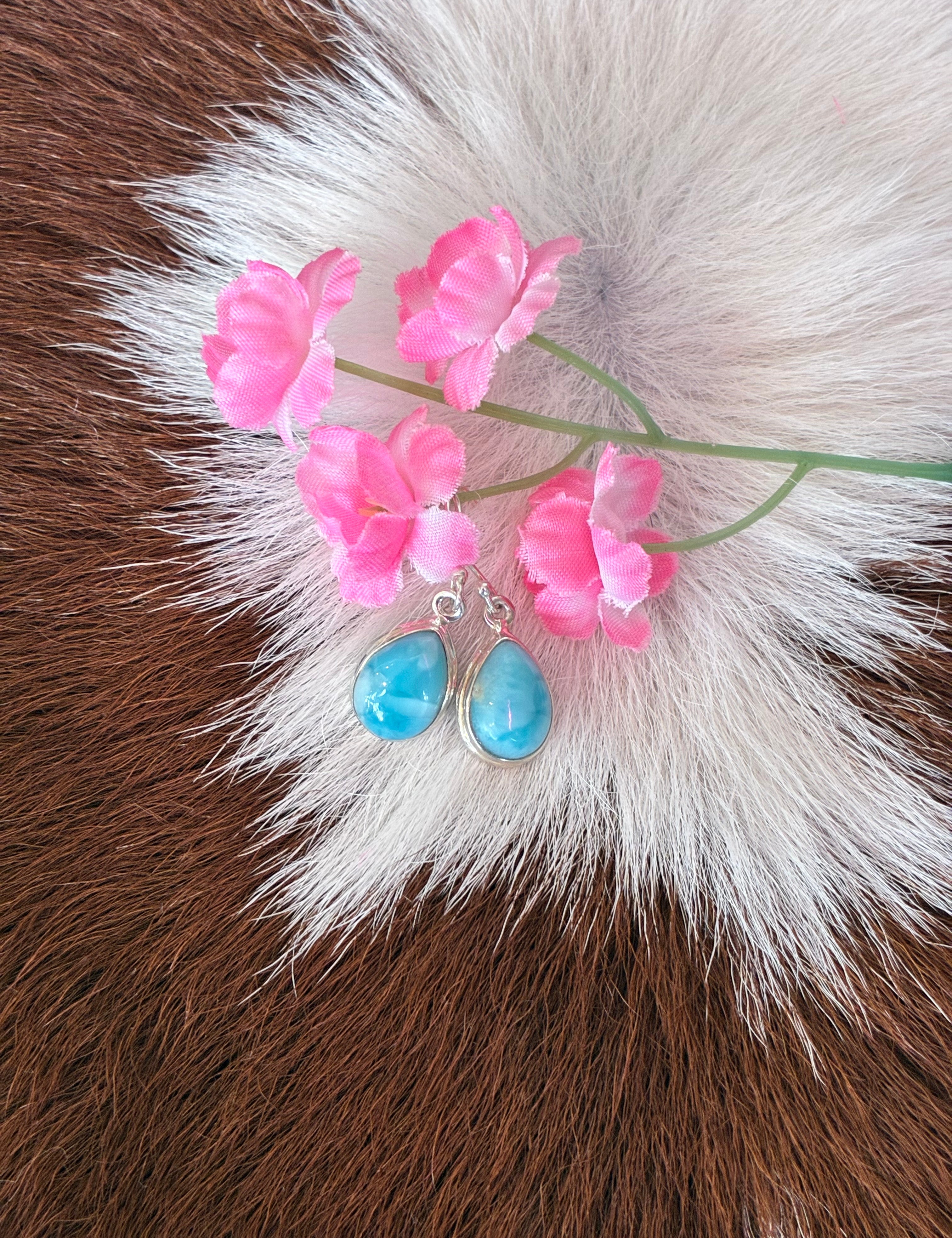 Teardrop Larimar earrings with vibrant blue hues set in silver, surrounded by pink flowers on a textured fur background.