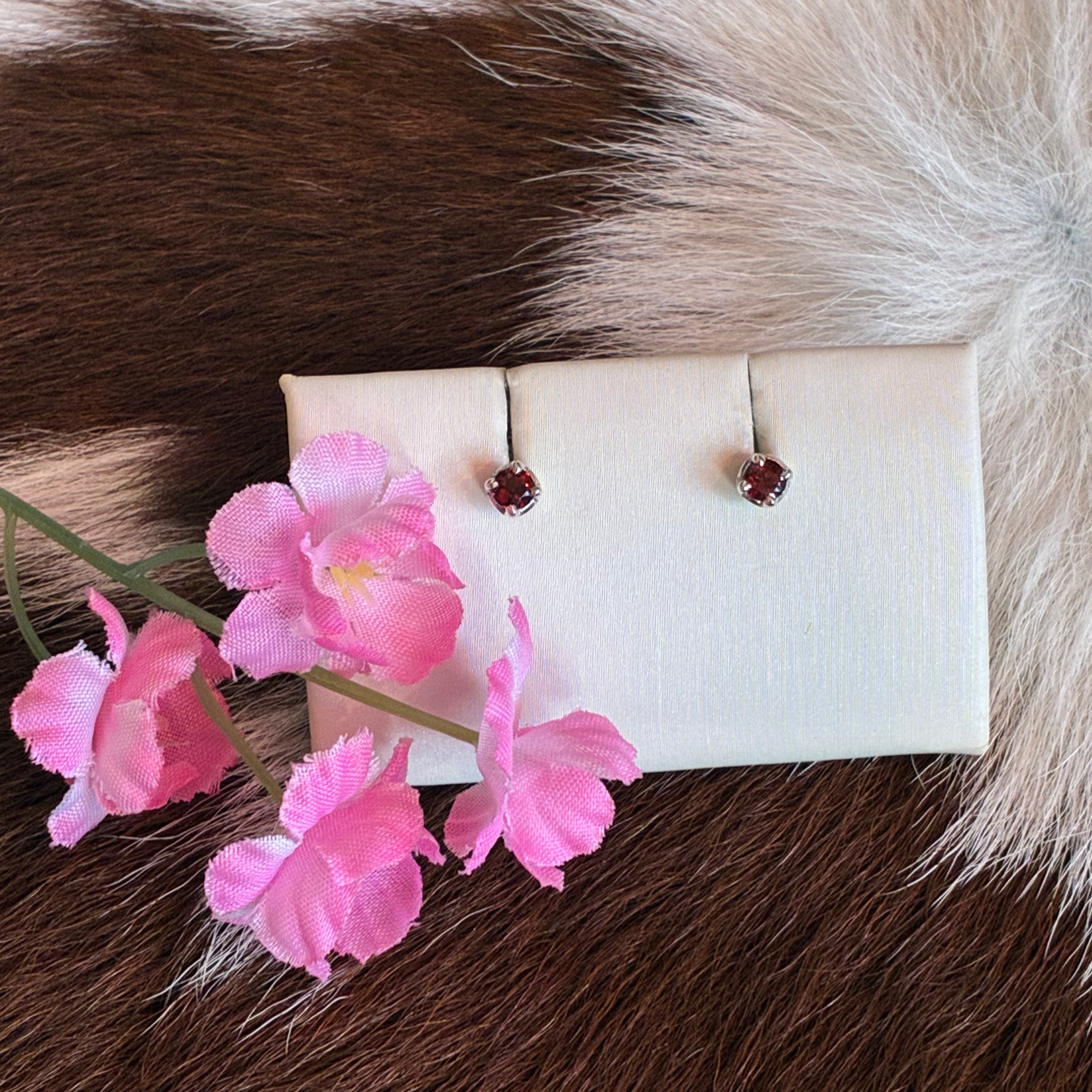 Pair of earrings on a white card with pink flowers on a fur background