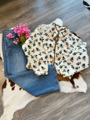 Floral-patterned cardigan over jeans on a wooden floor with pink flowers.