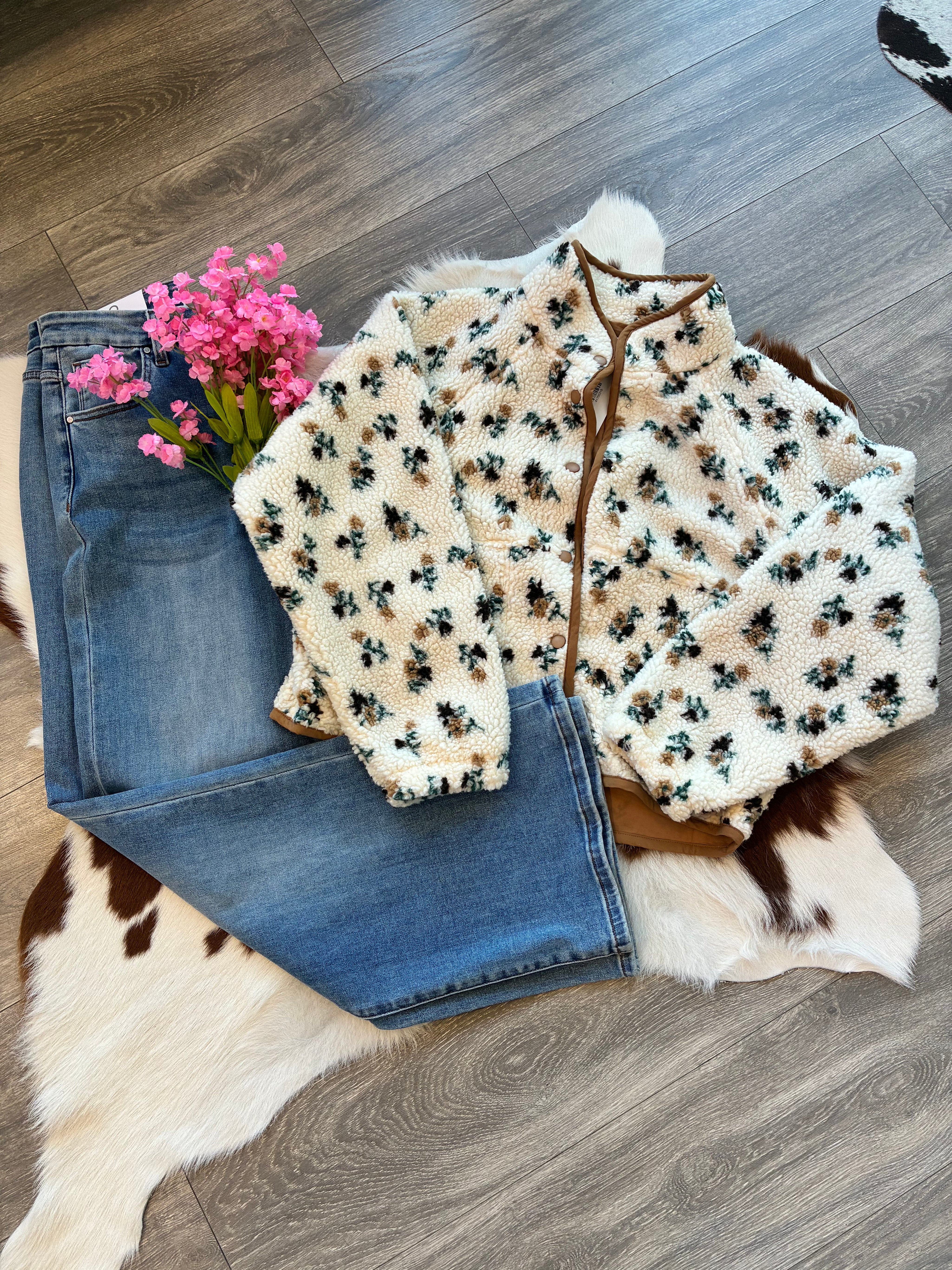 Floral-patterned cardigan over jeans on a wooden floor with pink flowers.