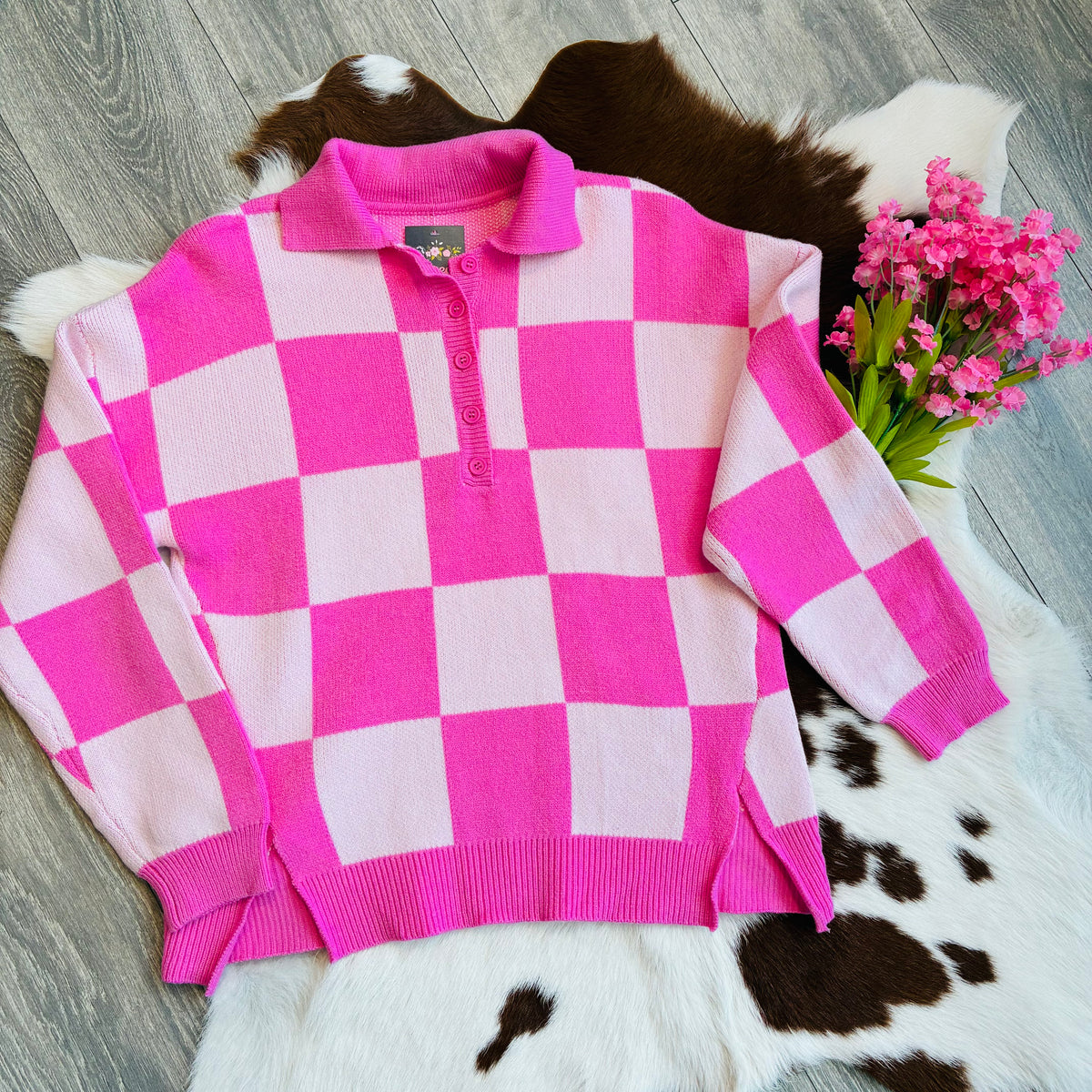 Pink and white checkered sweater on a wooden floor with a cowhide rug and pink flowers.