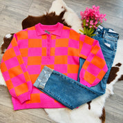 Pink and orange gingham polo sweater styled flat lay with cuffed distressed jeans and pink flowers on cowhide rug background