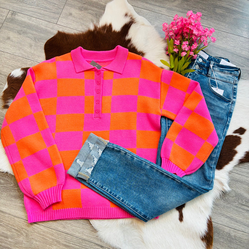 Pink and orange gingham polo sweater styled flat lay with cuffed distressed jeans and pink flowers on cowhide rug background