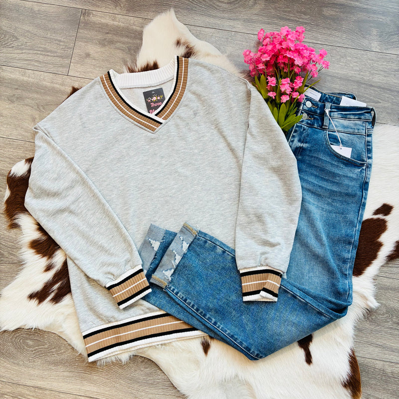 Gray sweater with brown and gold trim and blue jeans on a fur rug with pink flowers.