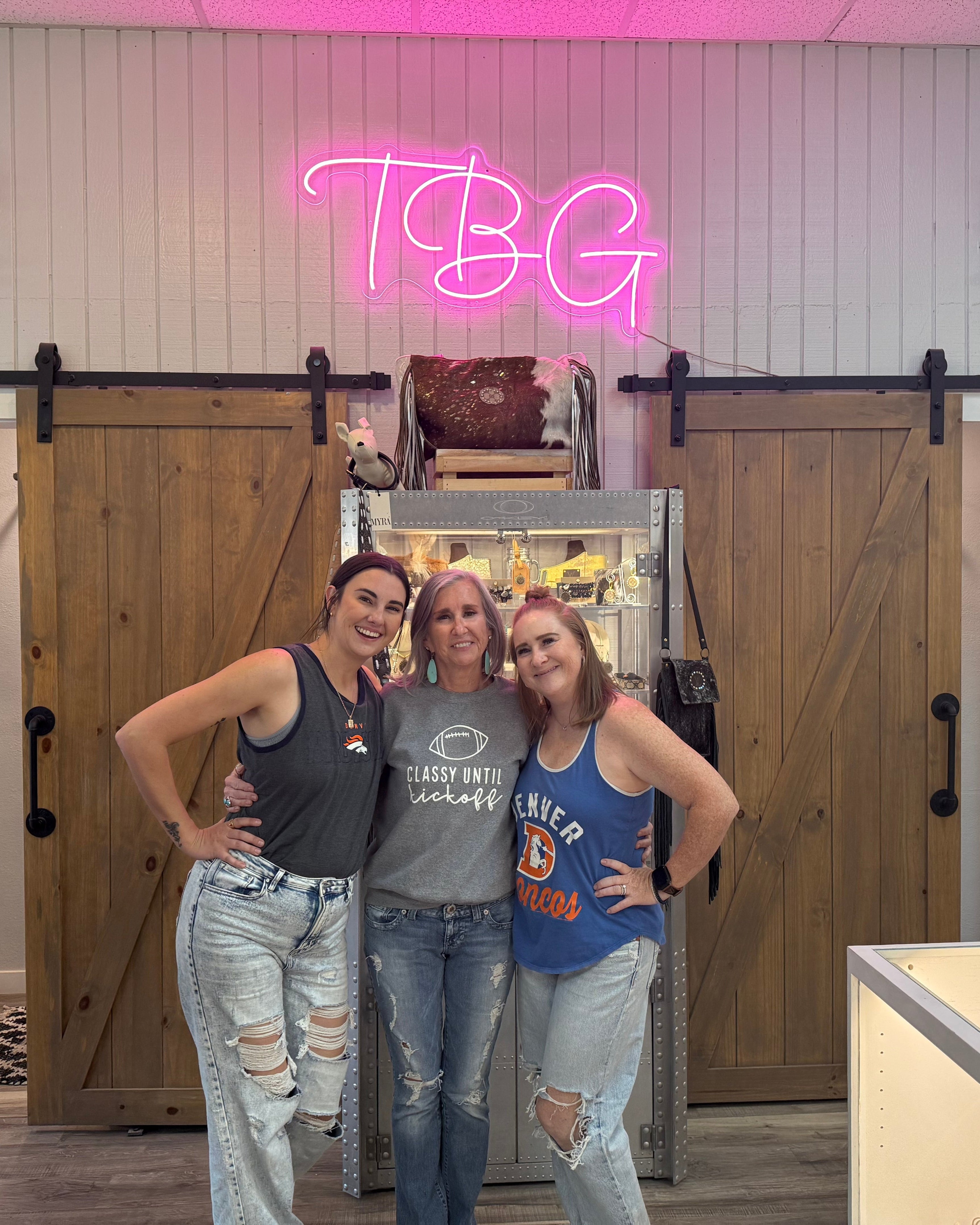 Three women posing in a store with a neon sign and clothing racks.