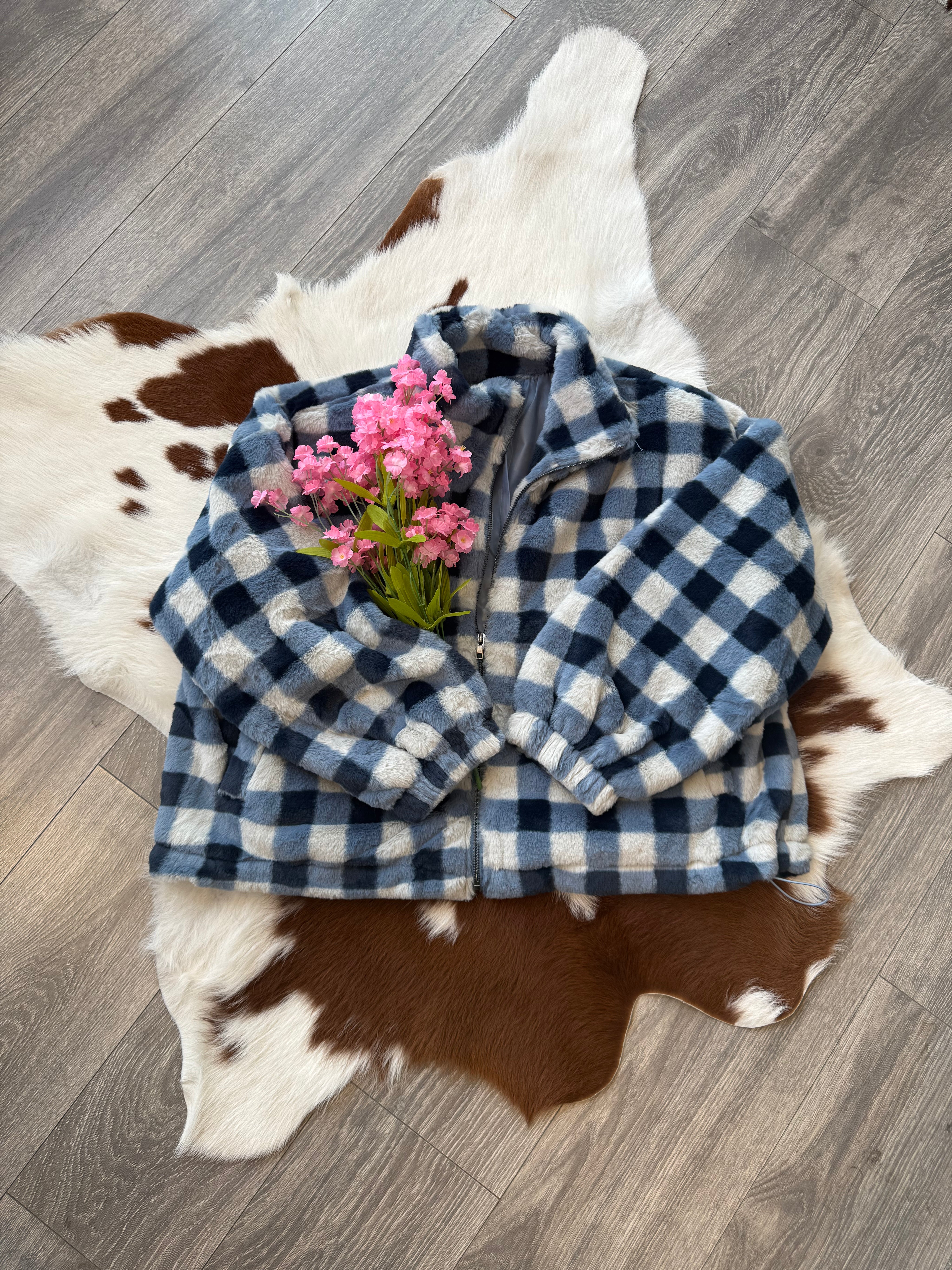 Cozy blue checkered fleece jacket displayed on a cowhide rug with pink flowers, showcasing a stylish and comfortable fashion piece.