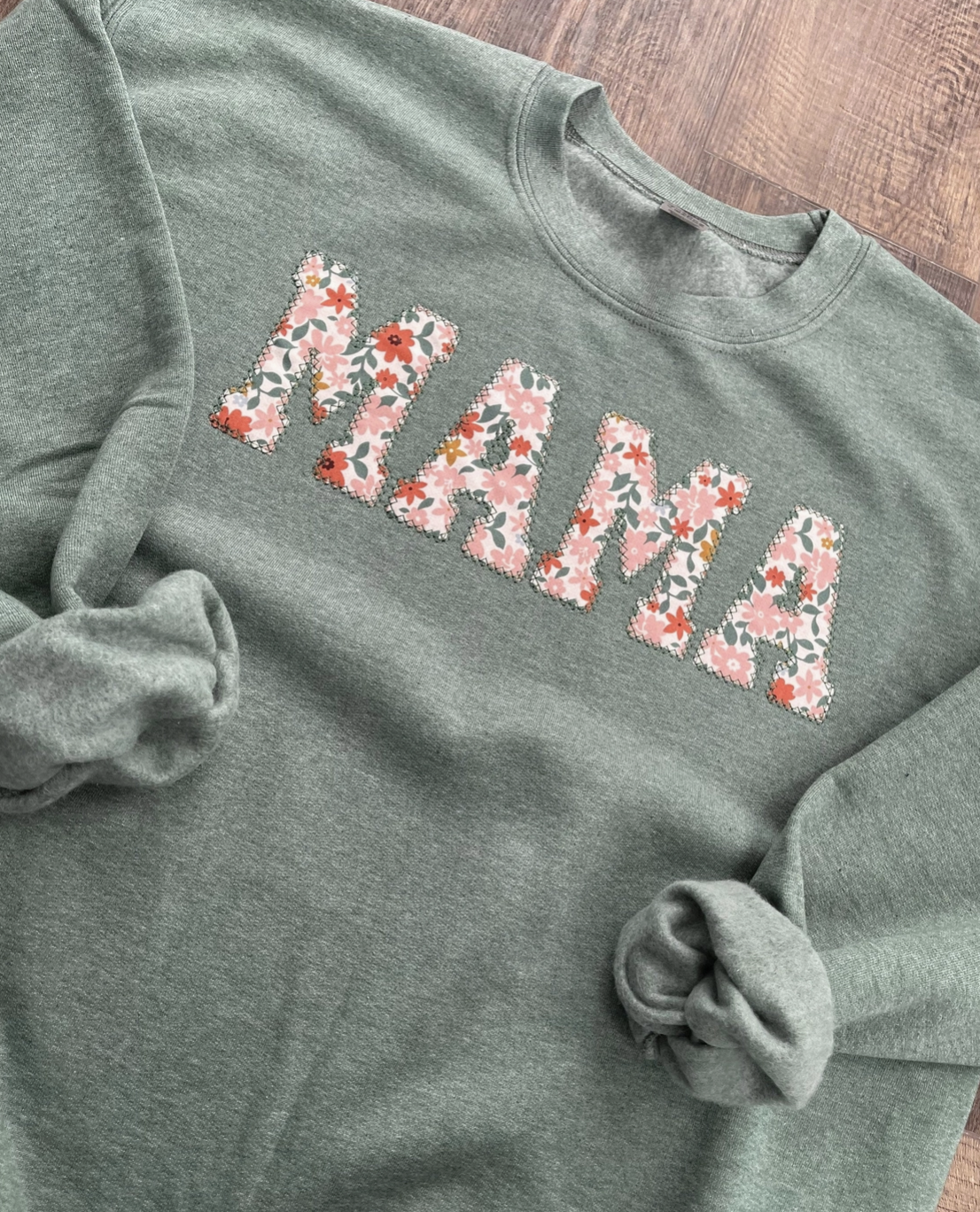 Sage green sweatshirt with 'MAMA' in floral applique letters, featuring a cozy relaxed fit and soft fabric, perfect for stylish moms and spring fashion.
