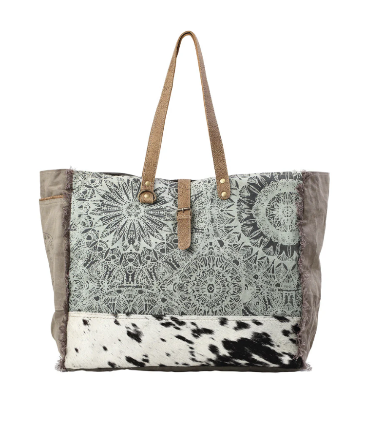 Green floral mandala print weekender tote with brown leather handles and a black-and-white cowhide panel on the bottom.

