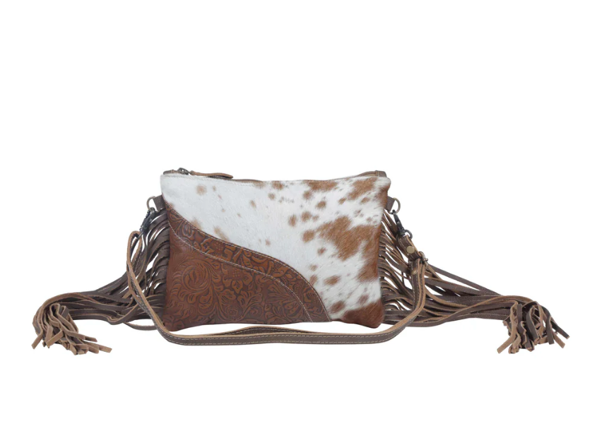 Western-style crossbody bag featuring brown tooled leather and speckled hair-on cowhide with fringe sides and adjustable strap.
