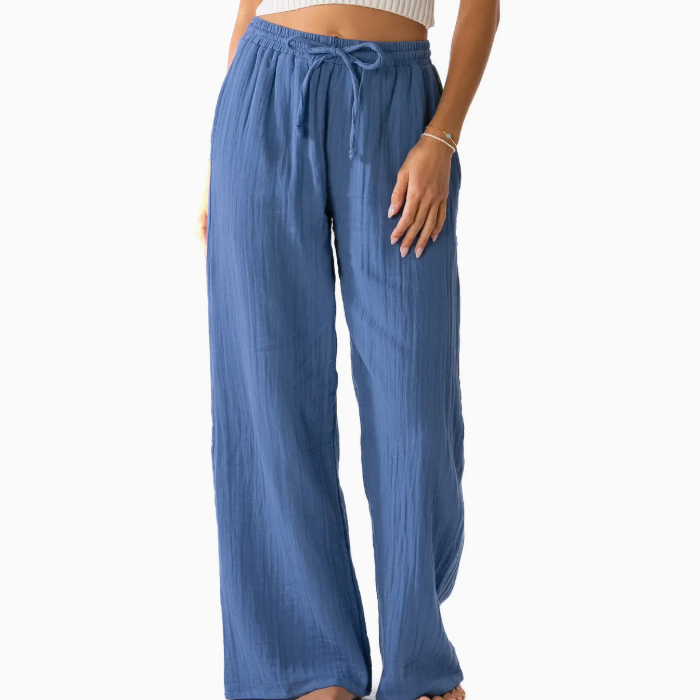 A woman wearing blue wide-leg pants with an adjustable drawstring waist, posing in a relaxed manner. She is paired with a fitted crop top, showcasing a casual and stylish look against a white background. The pants feature a flowy design, perfect for warm weather and comfortable outings.