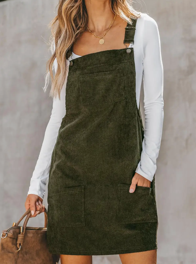 Model wearing an olive green corduroy overall dress layered over a white long-sleeve top, showcasing a stylish and casual fall look.