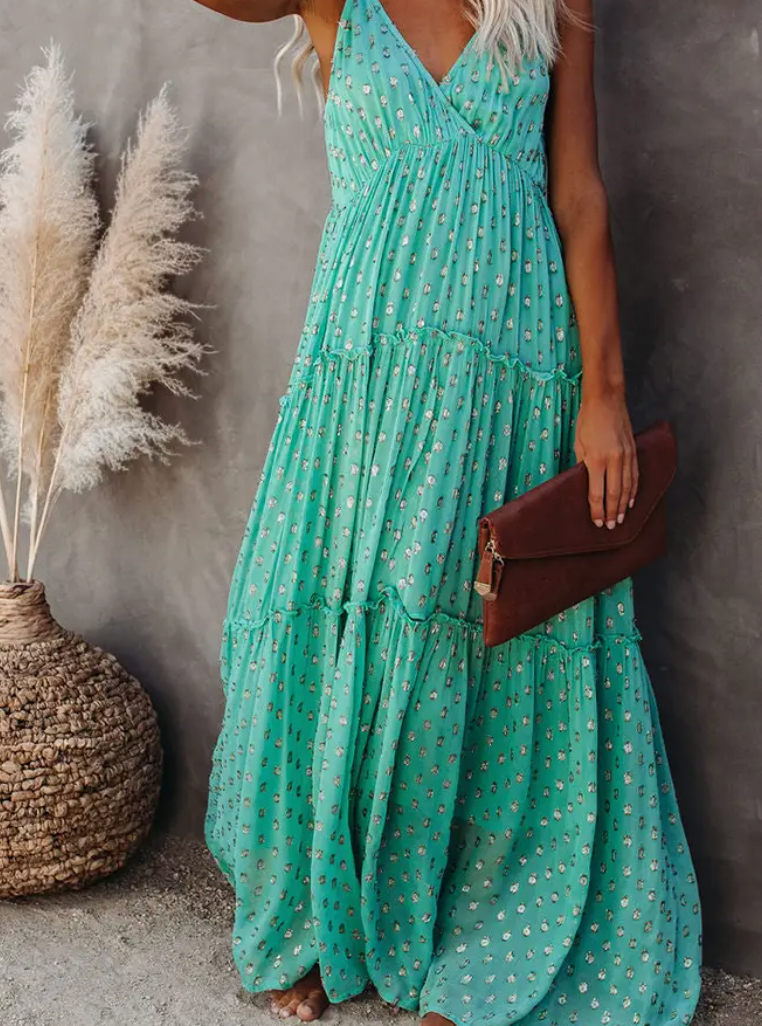 Woman wearing a mint green floral tiered maxi dress while holding a brown clutch, styled with boho decor and pampas grass in the background.

