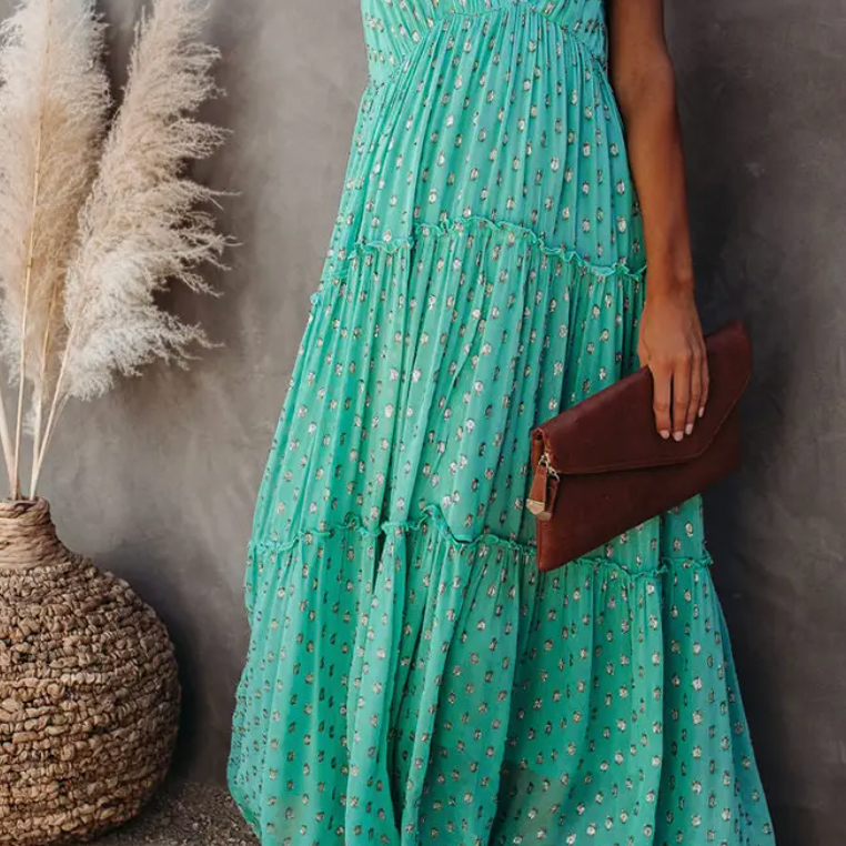 Woman wearing a mint green floral tiered maxi dress while holding a brown clutch, styled with boho decor and pampas grass in the background.

